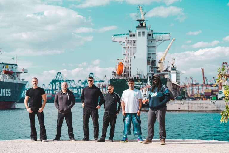 IOTA band members posing for a promotional photo at the port during daytime.
