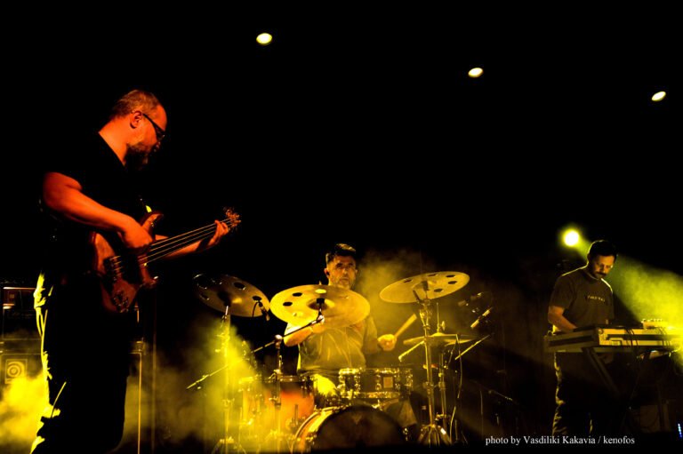 IOTA's bassist, keyboardist and drummer performing live on stage.