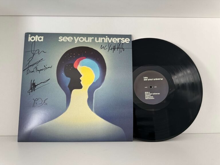 Signed vinyl copy of IOTA's album *See Your Universe* with black vinyl and cover, displayed against a white wall.