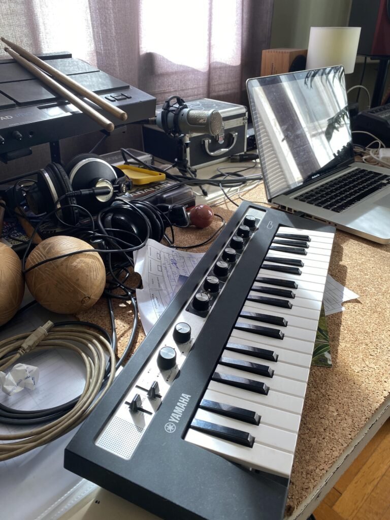 Yamaha Clavinova, laptop, electronic drum pads, headphones, and microphone setup in studio