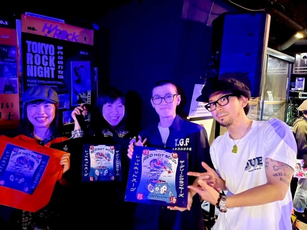 Four Green Flyers members showing band merch and vinyl album