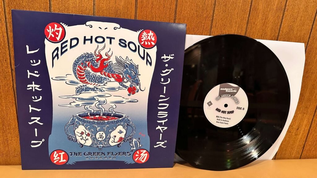 The Green Flyers – Red Hot Soup vinyl record and cover on a wooden wall