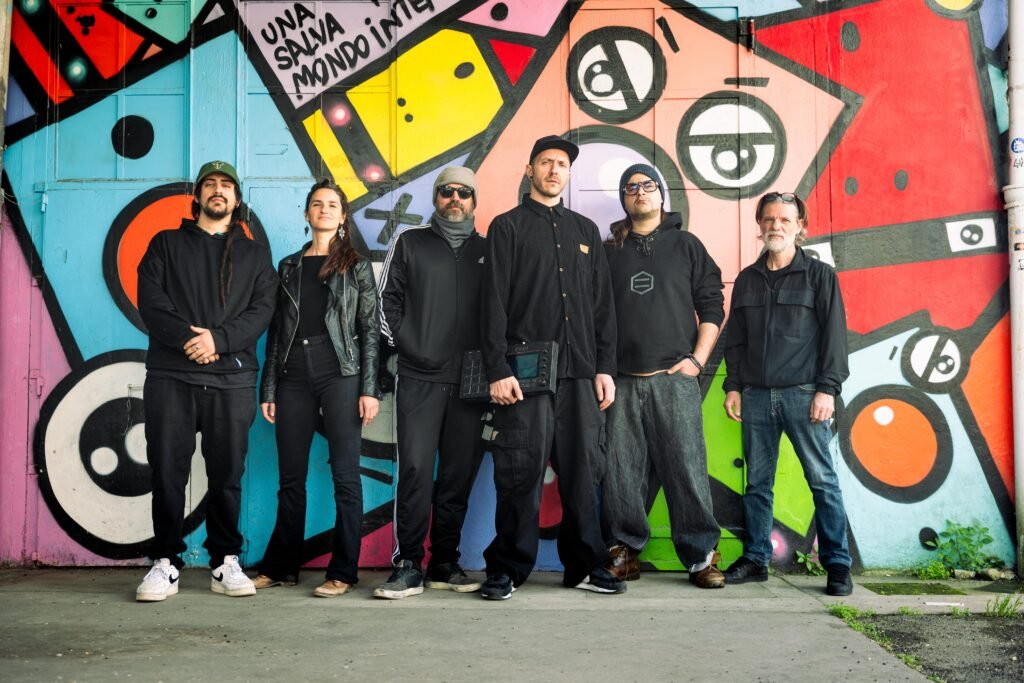 Flexional duo with session musicians posing at graffiti wall, one holding MPC One sampler