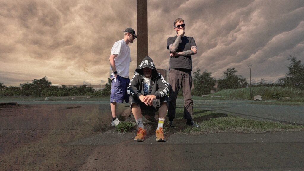 Real Juice band members posing outdoors in an industrial location under dramatic clouds